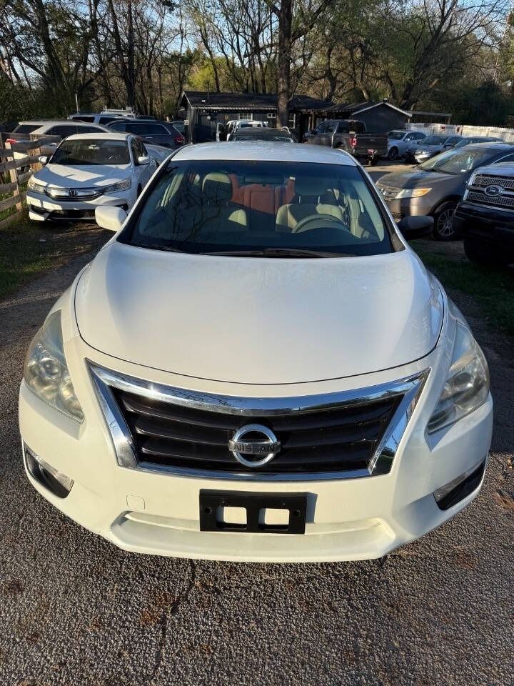 White Nissan sedan parked in a lot, front view, with other cars in the background.