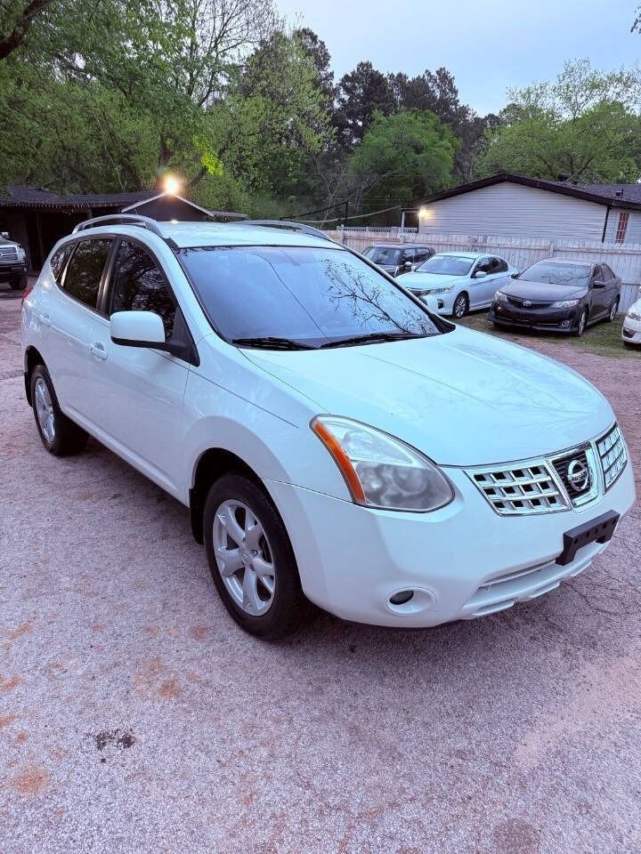 White Nissan SUV parked on a gravel lot near trees and other cars at dusk
