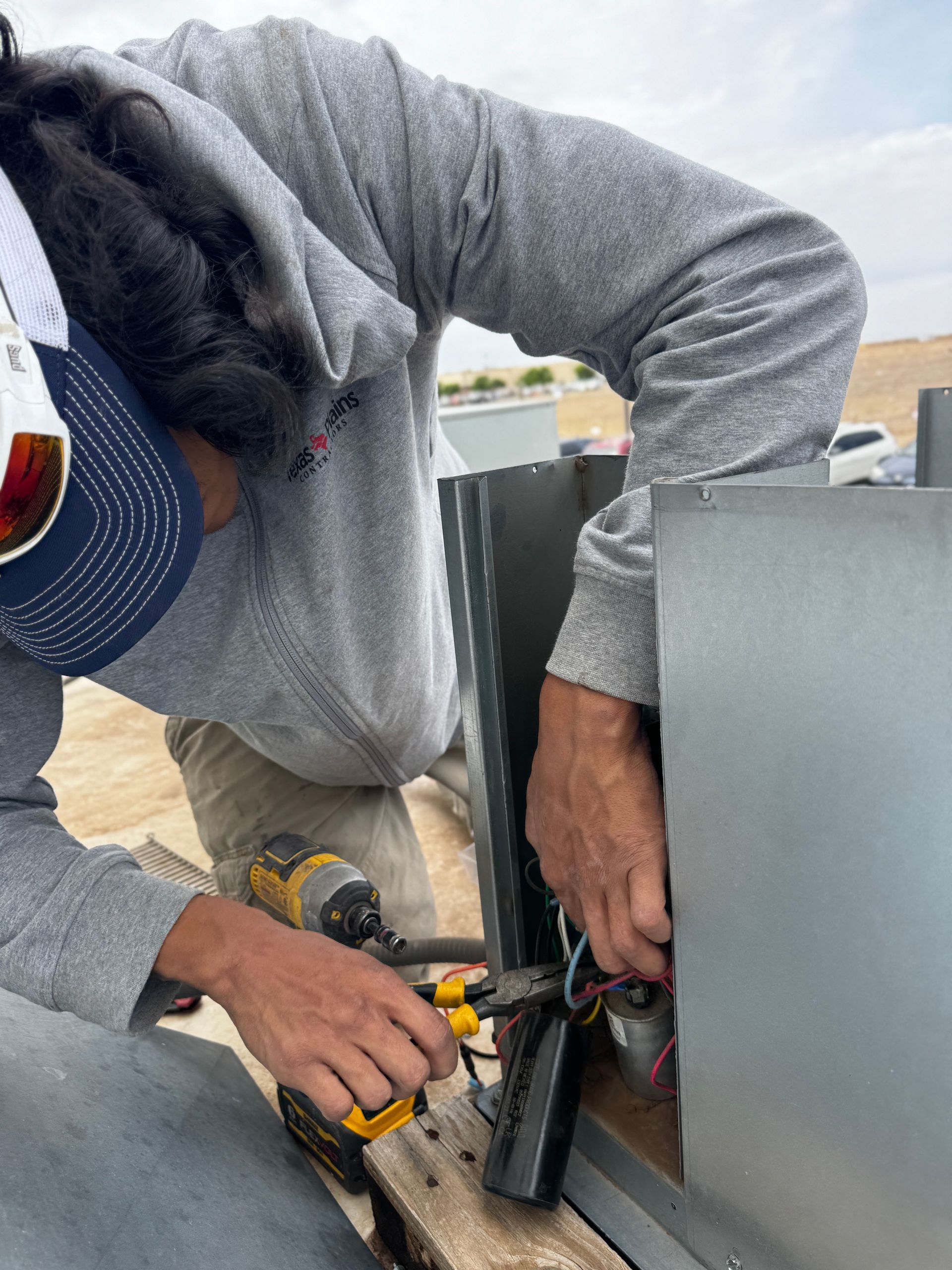 Two technicians in work hoodies and caps repair an indoor HVAC furnace unit.