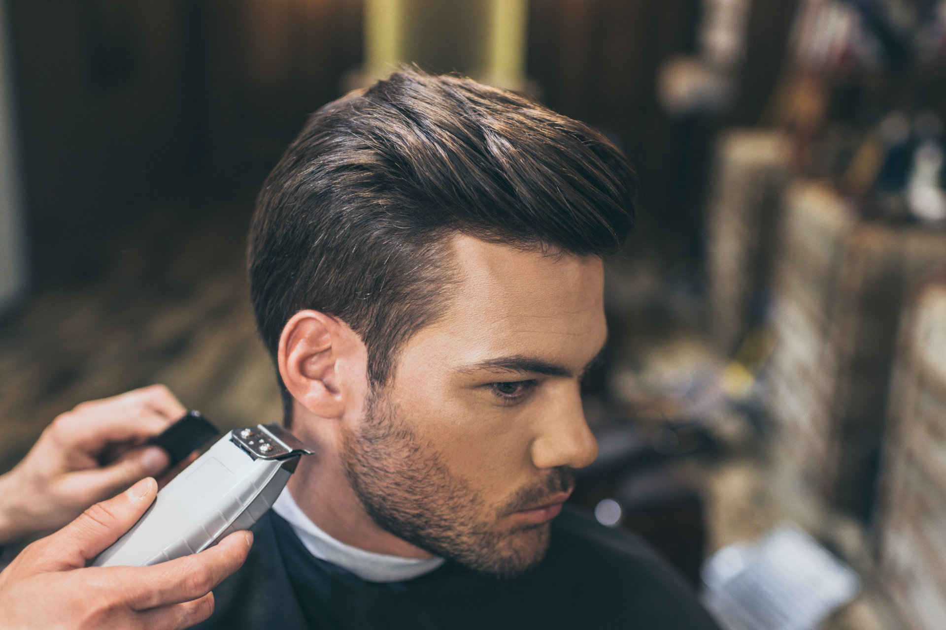 Barber trimming a man’s hair with clippers in a salon