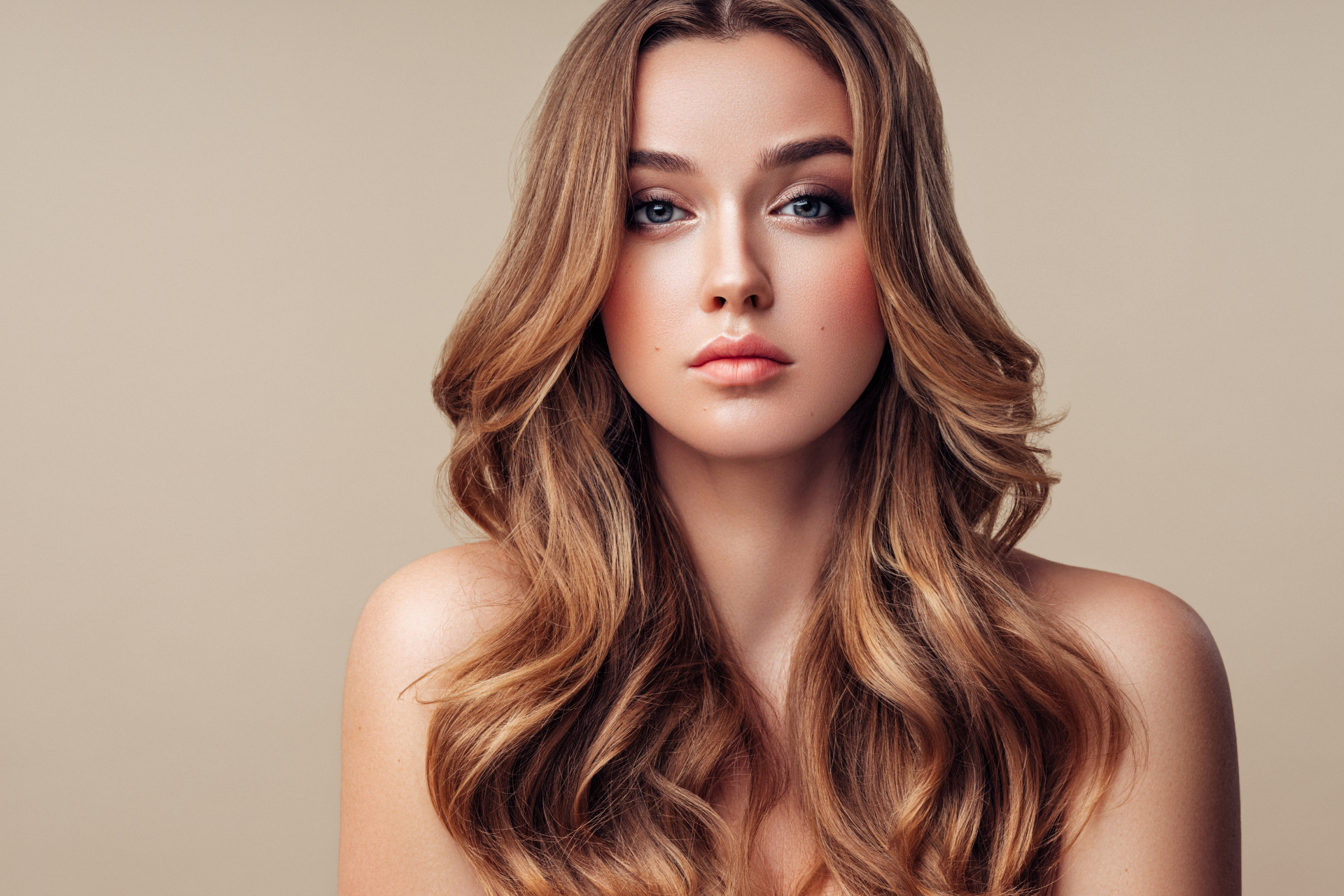 Studio portrait of a person with long wavy brown hair against a beige background