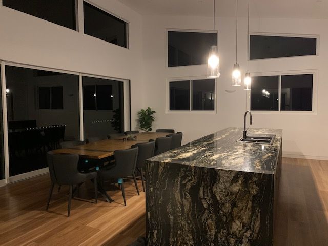 Modern Kitchen With Granite Island, Wood Table, and High Windows — Rob Ward Electrical Services in Mullumbimby, NSW
