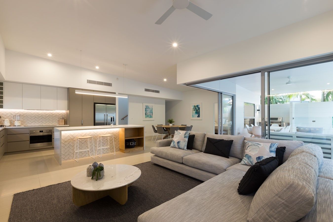 Open-plan living room with kitchen island, sectional sofa, and sliding glass doors to a patio— Rob Ward Electrical Services in West Ballina, NSW