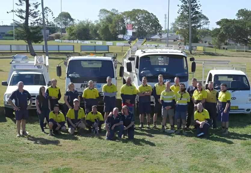 A Group of Electricians Posing for a Picture With Trucks in the Background — Rob Ward Electrical Services in West Ballina, NSW