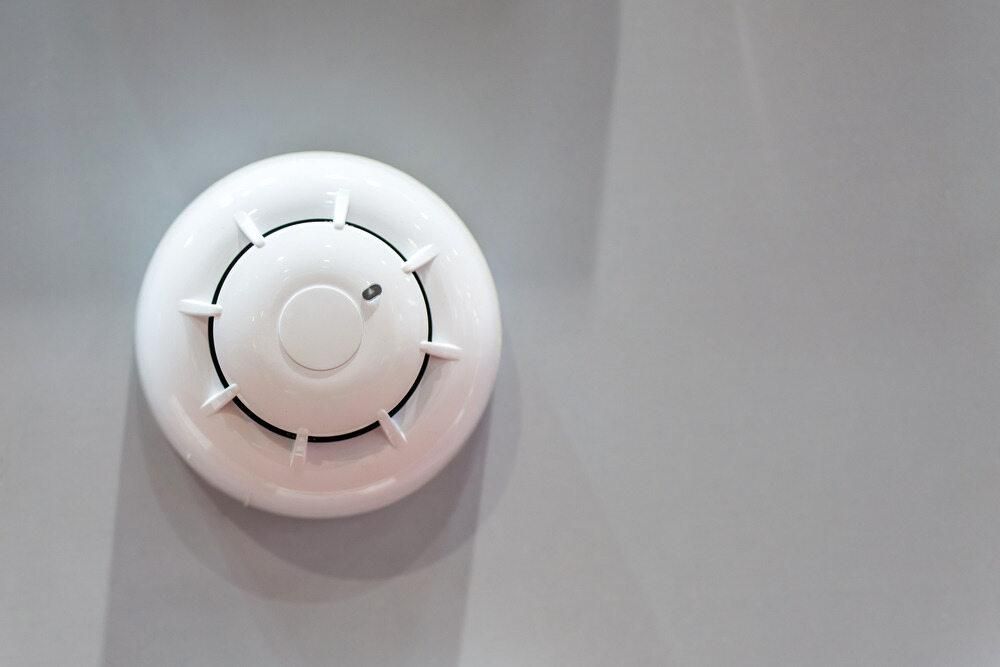 A White Smoke Detector is Mounted on a Gray Wall — Rob Ward Electrical Services in Lennox Head, NSW