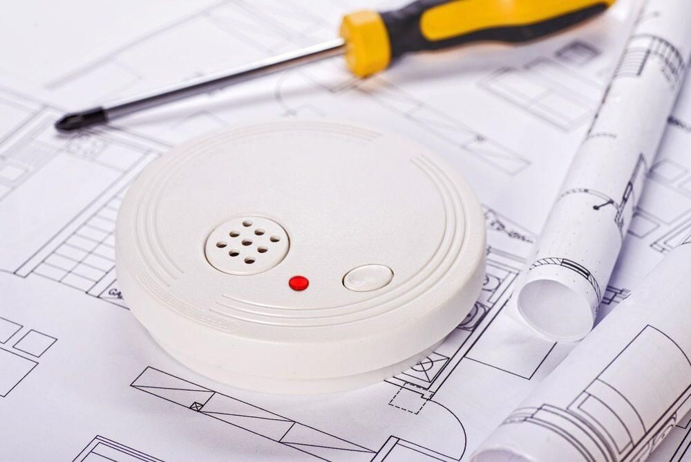 A Smoke Detector is Sitting on Top of a Blueprint Next to a Screwdriver — Rob Ward Electrical Services in Kingscliff, NSW