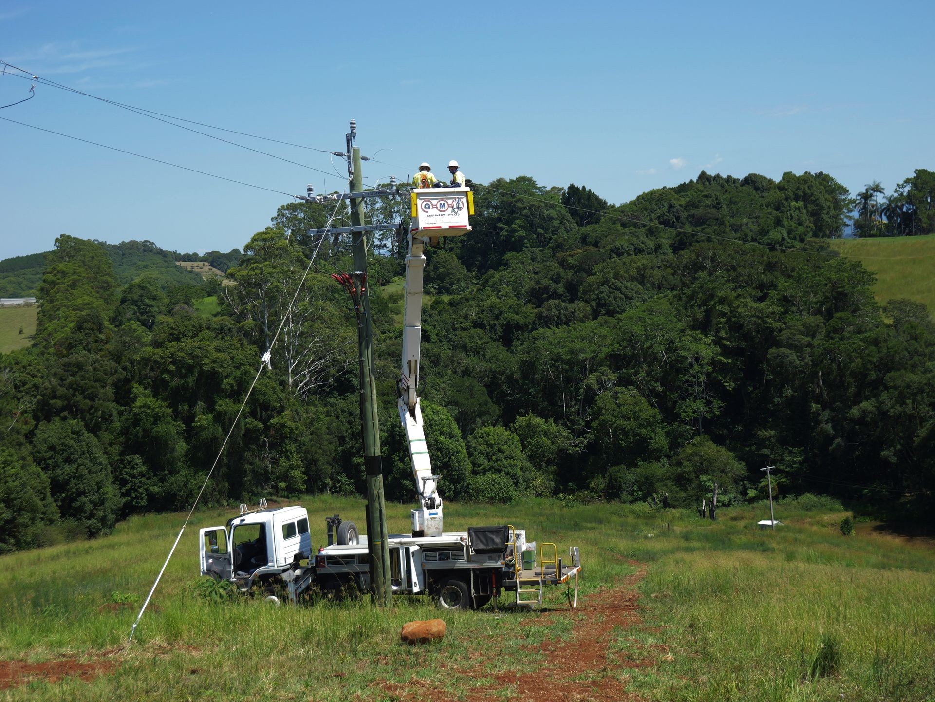 Utility Workers in a Bucket Truck Servicing Power Lines on a Grassy Hill — Rob Ward Electrical Services in Broadwater, NSW