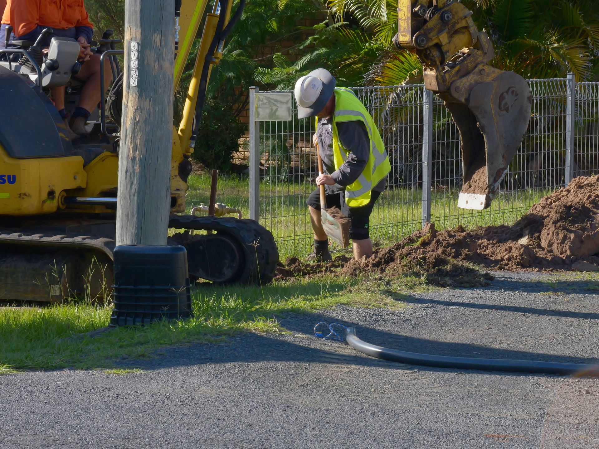 Construction worker in reflective vest digging near an excavator and power pole— Rob Ward Electrical Services in West Ballina, NSW