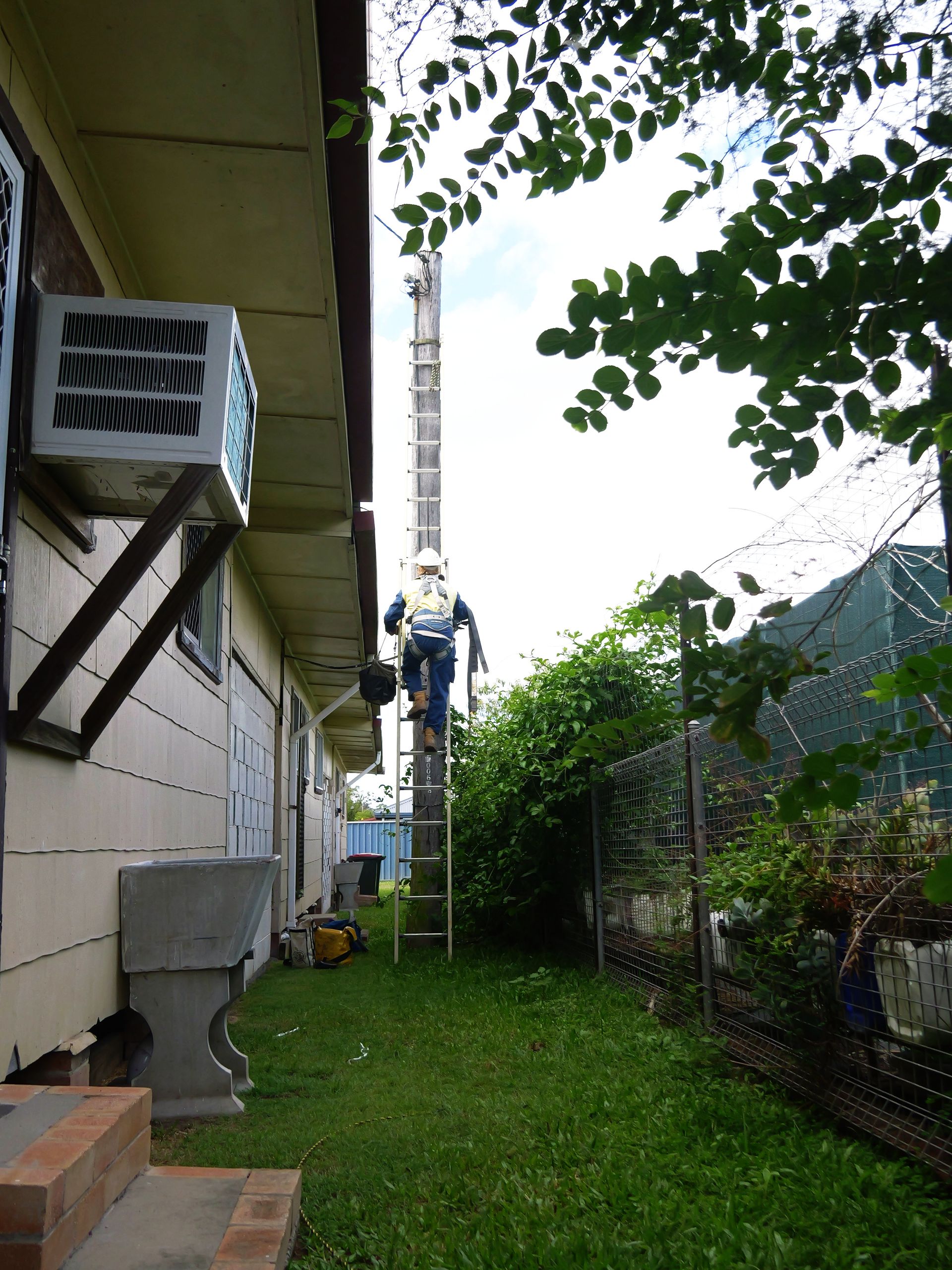 Person Climbing a Tall Ladder Next to a House — Rob Ward Electrical Services in Lismore, NSW