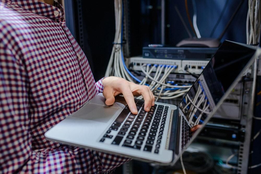 A Man is Using a Laptop Computer in a Server Room — Rob Ward Electrical Services in Wollongbar, NSW