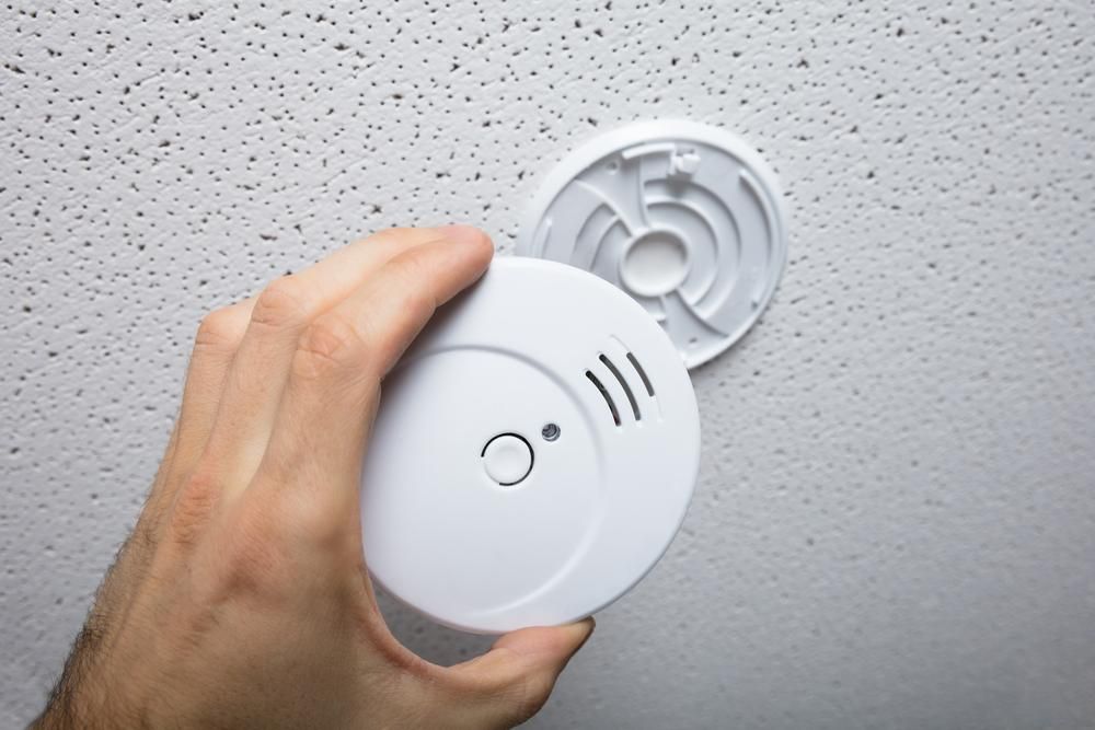A Person is Installing a Smoke Detector on the Ceiling — Rob Ward Electrical Services in Lismore, NSW