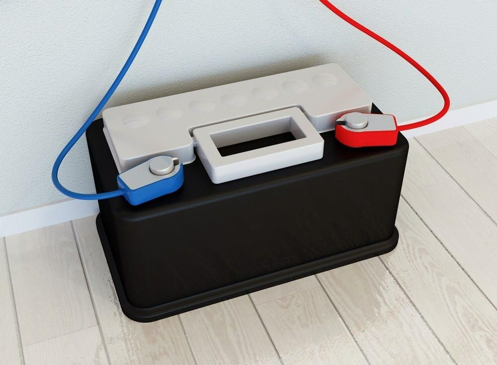 A Battery With Two Wires Attached to It is Sitting on a Wooden Floor — Rob Ward Electrical Services in Mullumbimby, NSW
