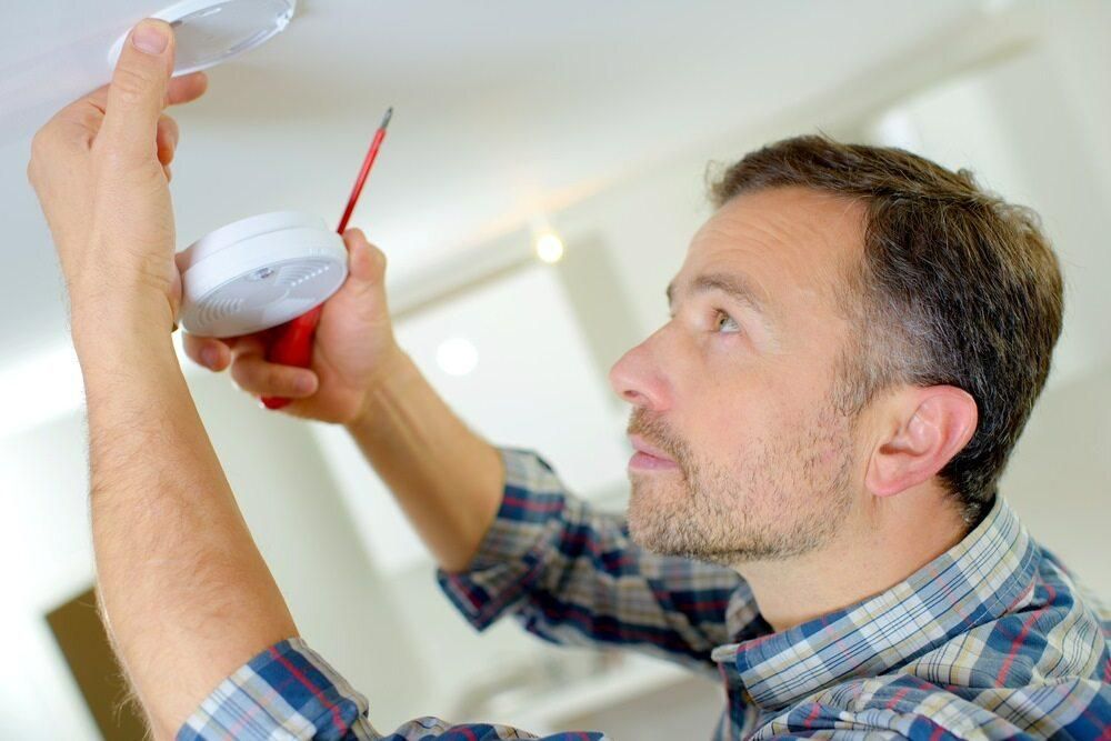 A Man is Installing a Smoke Detector on the Ceiling — Rob Ward Electrical Services in Wardell, NSW