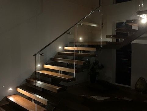 A Wooden Staircase With a Glass Railing in a Dark Room — Rob Ward Electrical Services in West Ballina, NSW