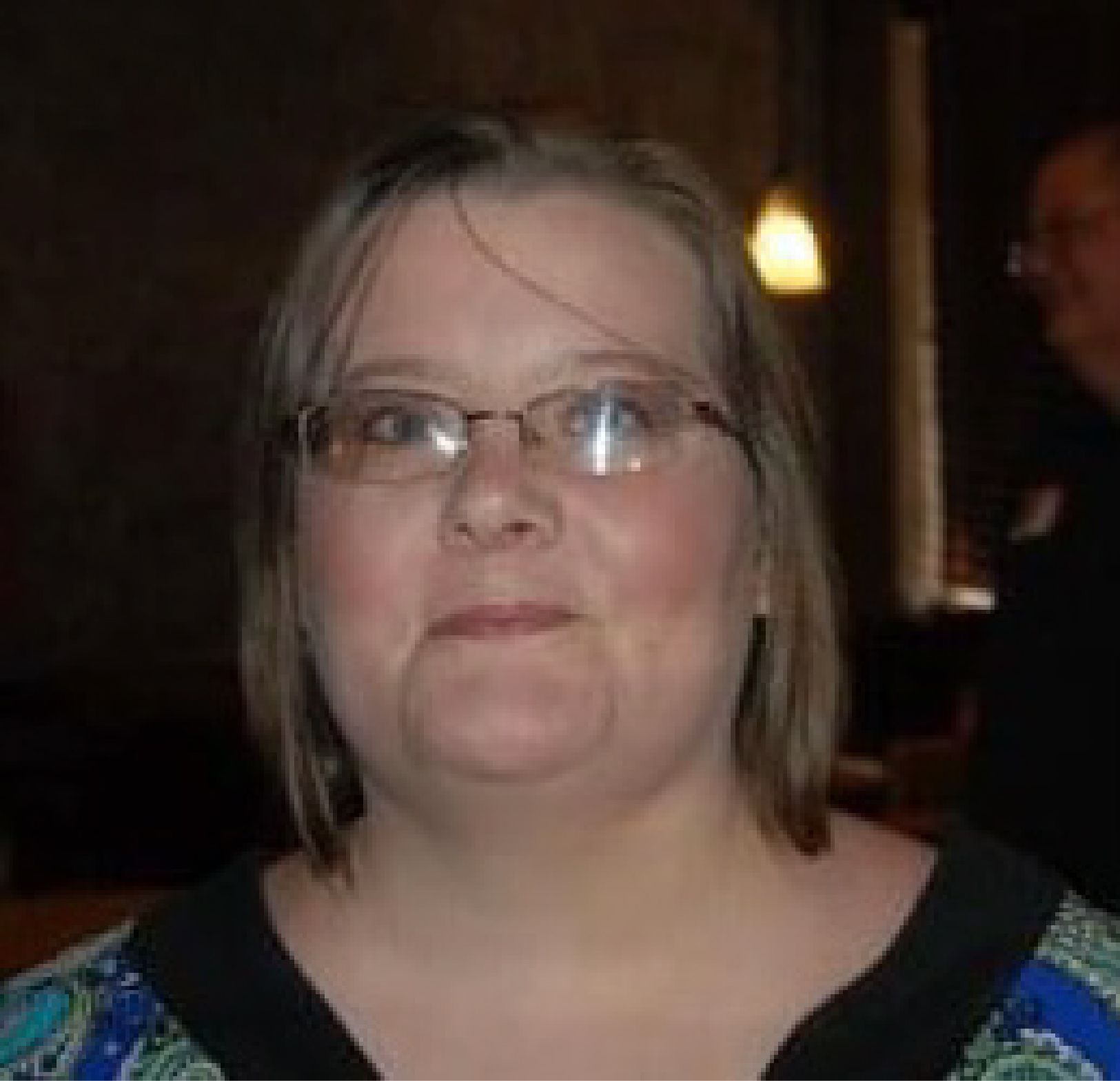 A woman wearing glasses and a blue shirt is looking at the camera.