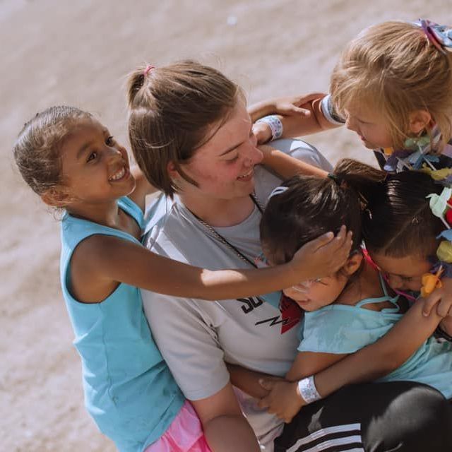 A woman wearing a shirt that says ' sd ' on it is hugging three little girls