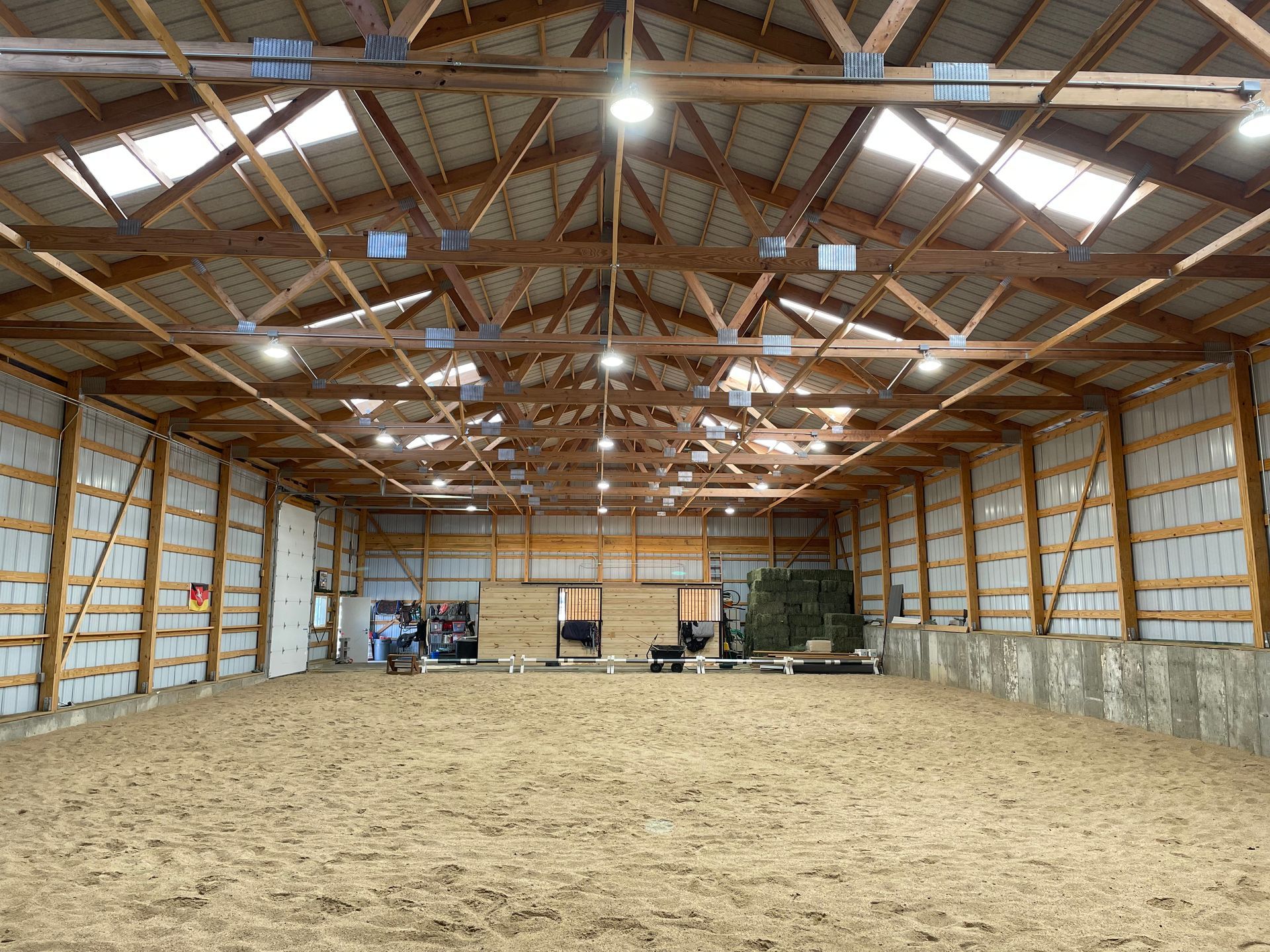 Indoor riding arena, sand floor, wooden rafters, skylights, white walls.