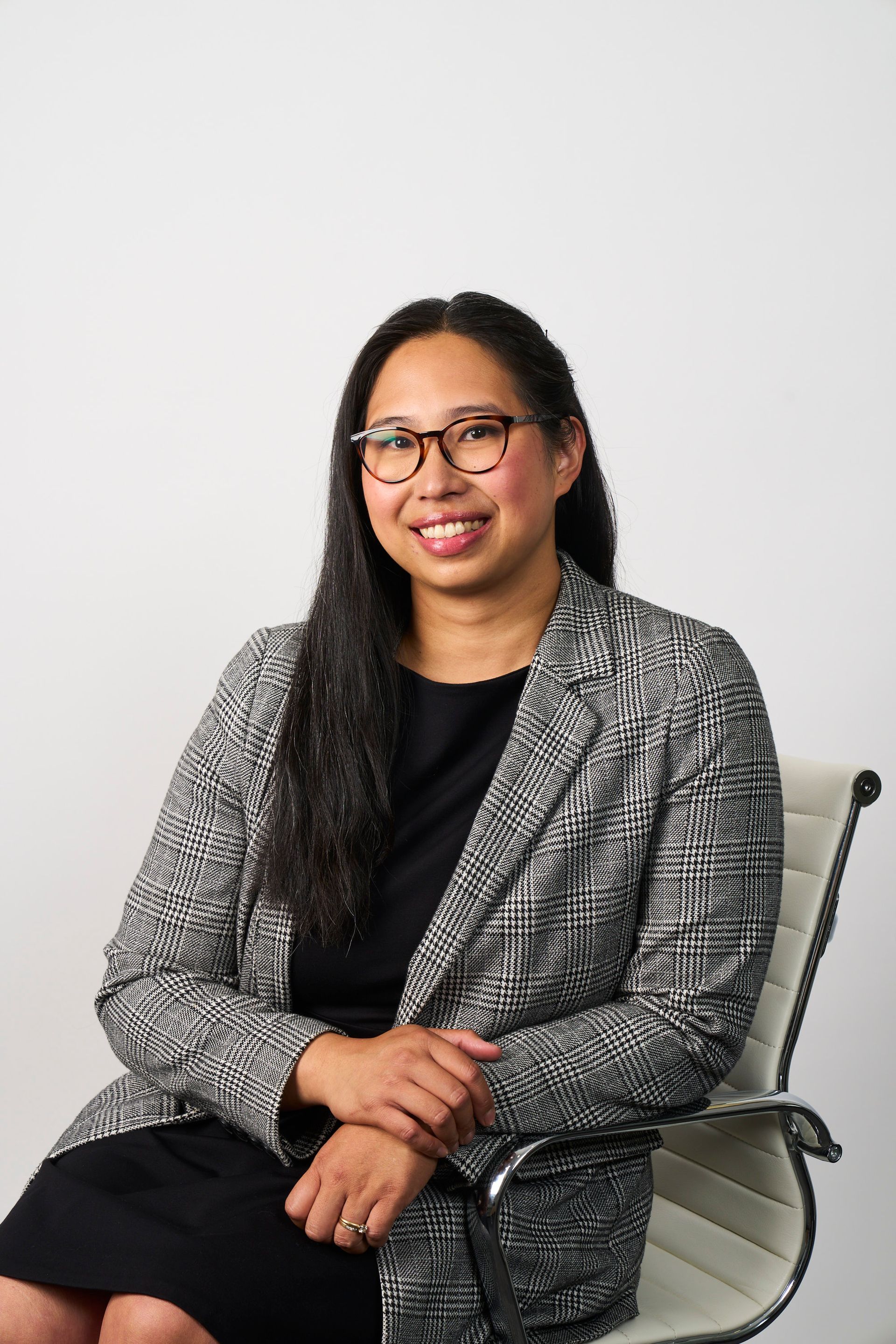 A woman with long dark hair and glasses wearing a black top and patterned blazer