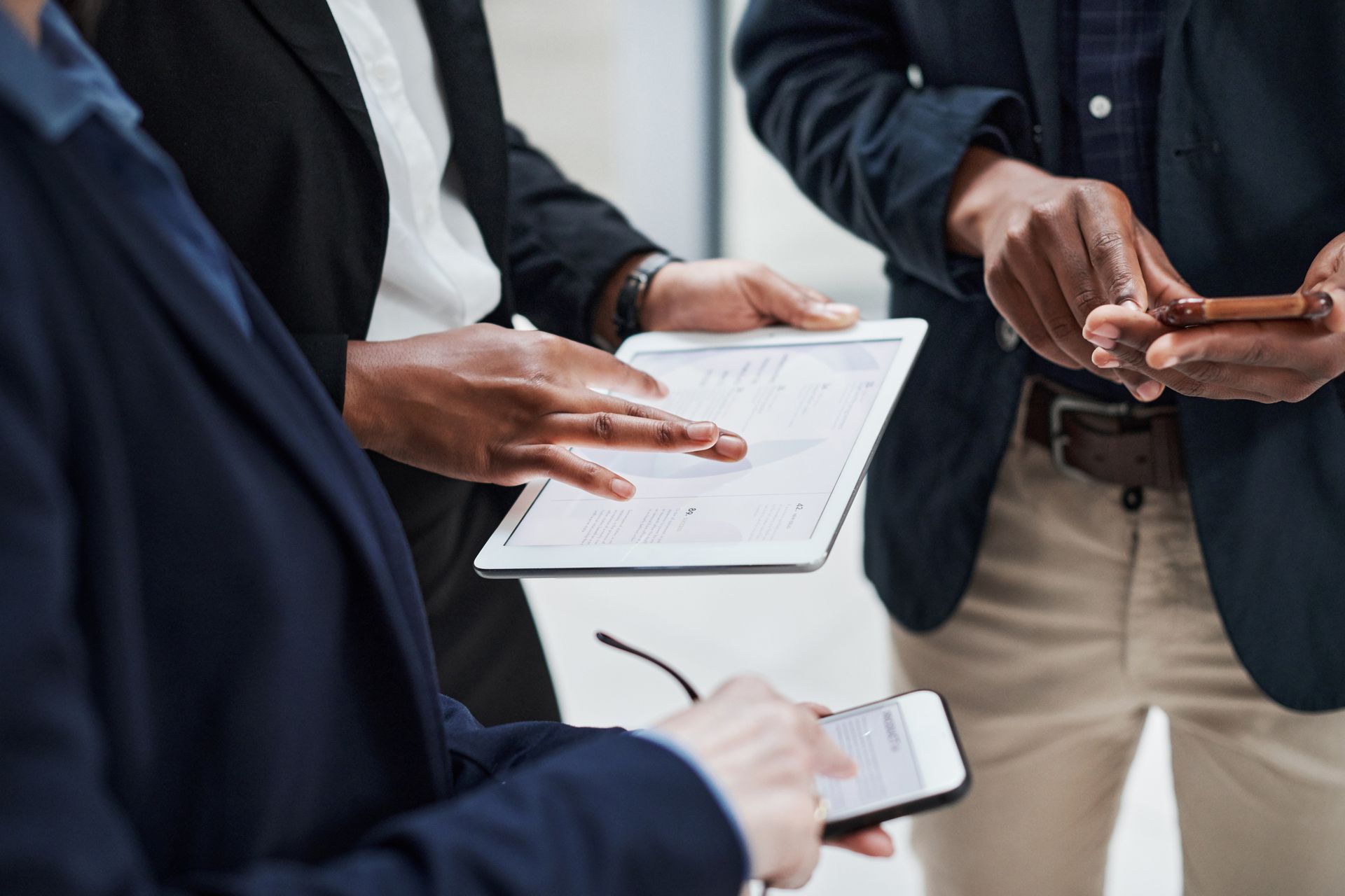 Three business professionals in formal attire collaborating while using a digital tablet and a smartphone
