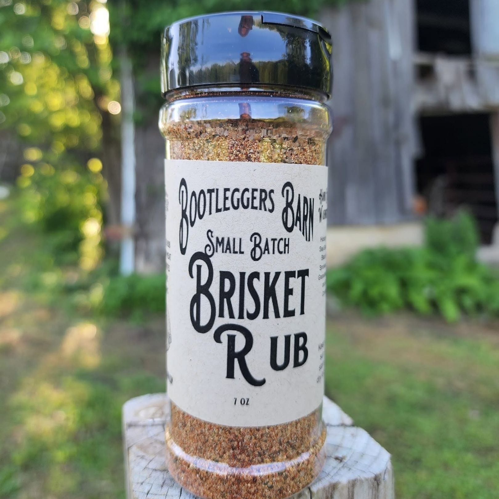 Bottle of Bootlegger's small batch Brisket Rub seasoning on a wooden post outdoors