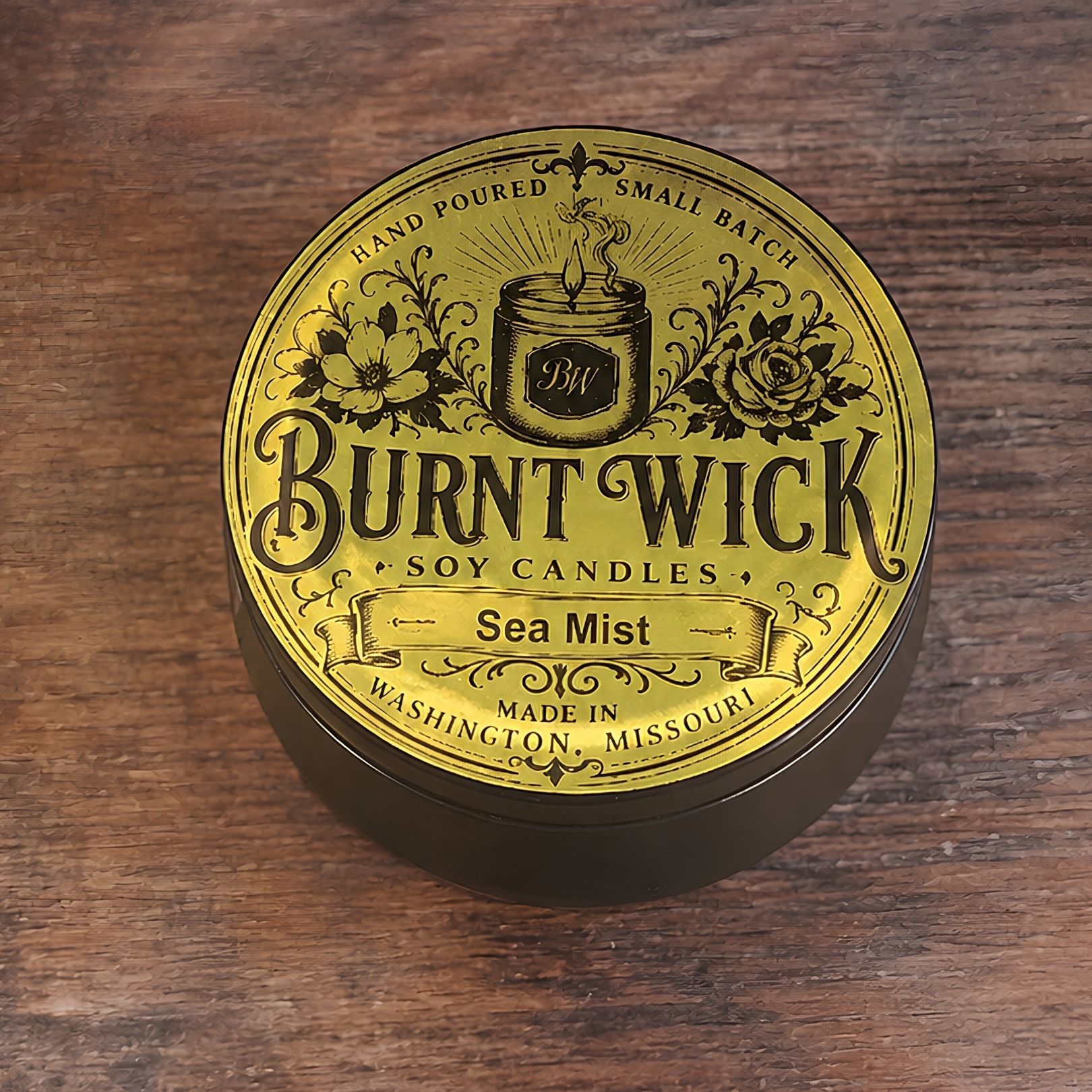 Round gold Burnt Wick soy candle tin labeled “Sea Mist” on a wooden surface.