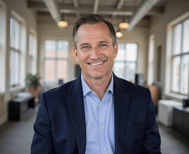 A man in a suit and blue shirt is smiling in an office.