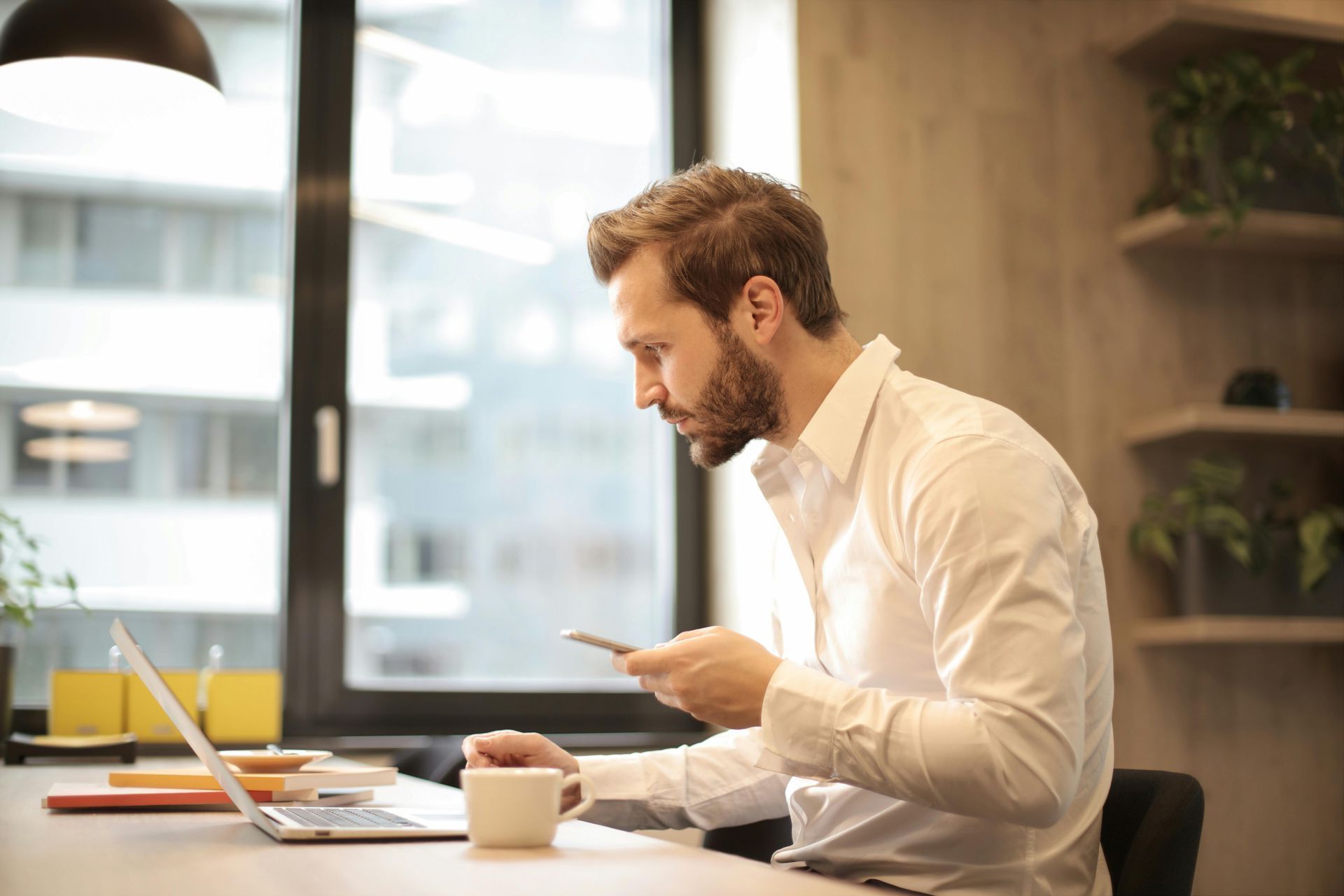 A man is sitting at a table using a laptop and a cell phone.