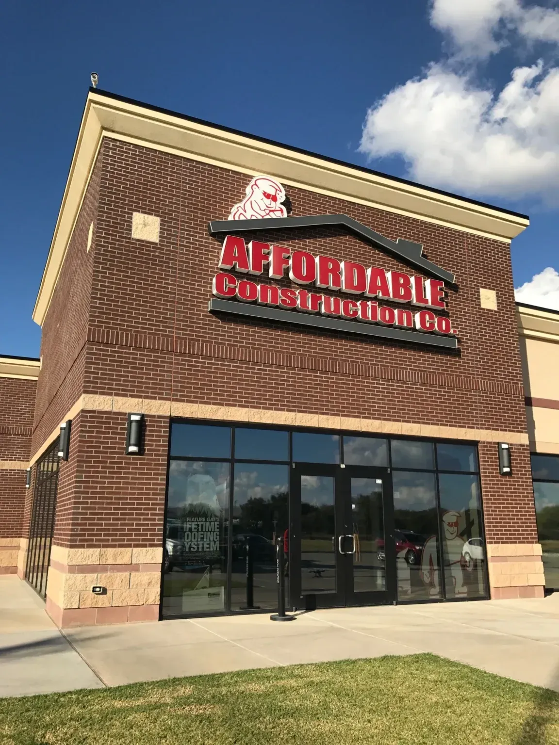 Affordable Computers storefront with brick facade, red sign, glass doors, and grassy sidewalk under blue sky