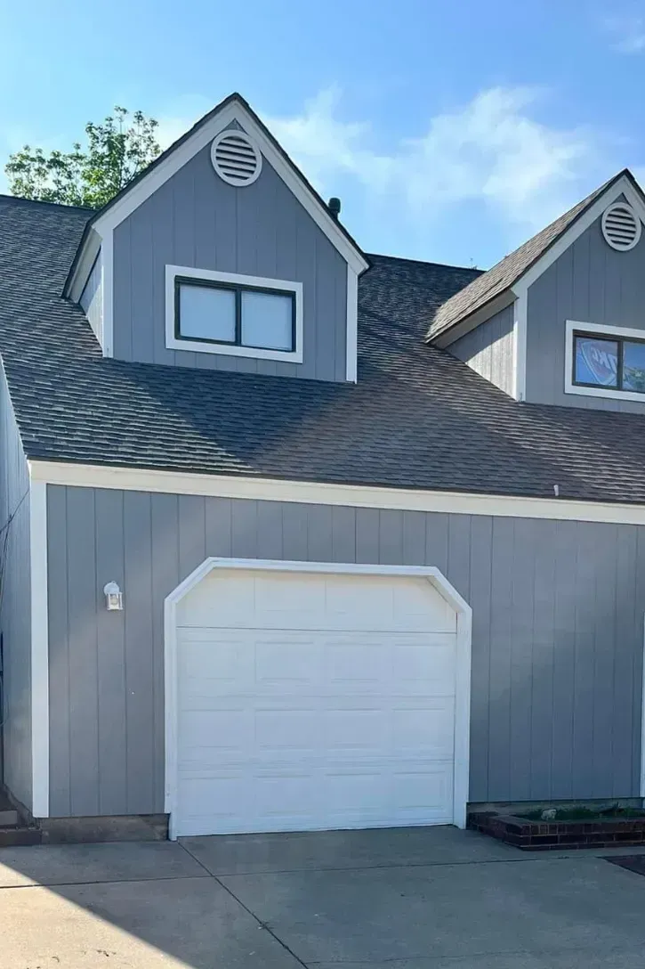Gray townhouse with white garage door and blue sky.