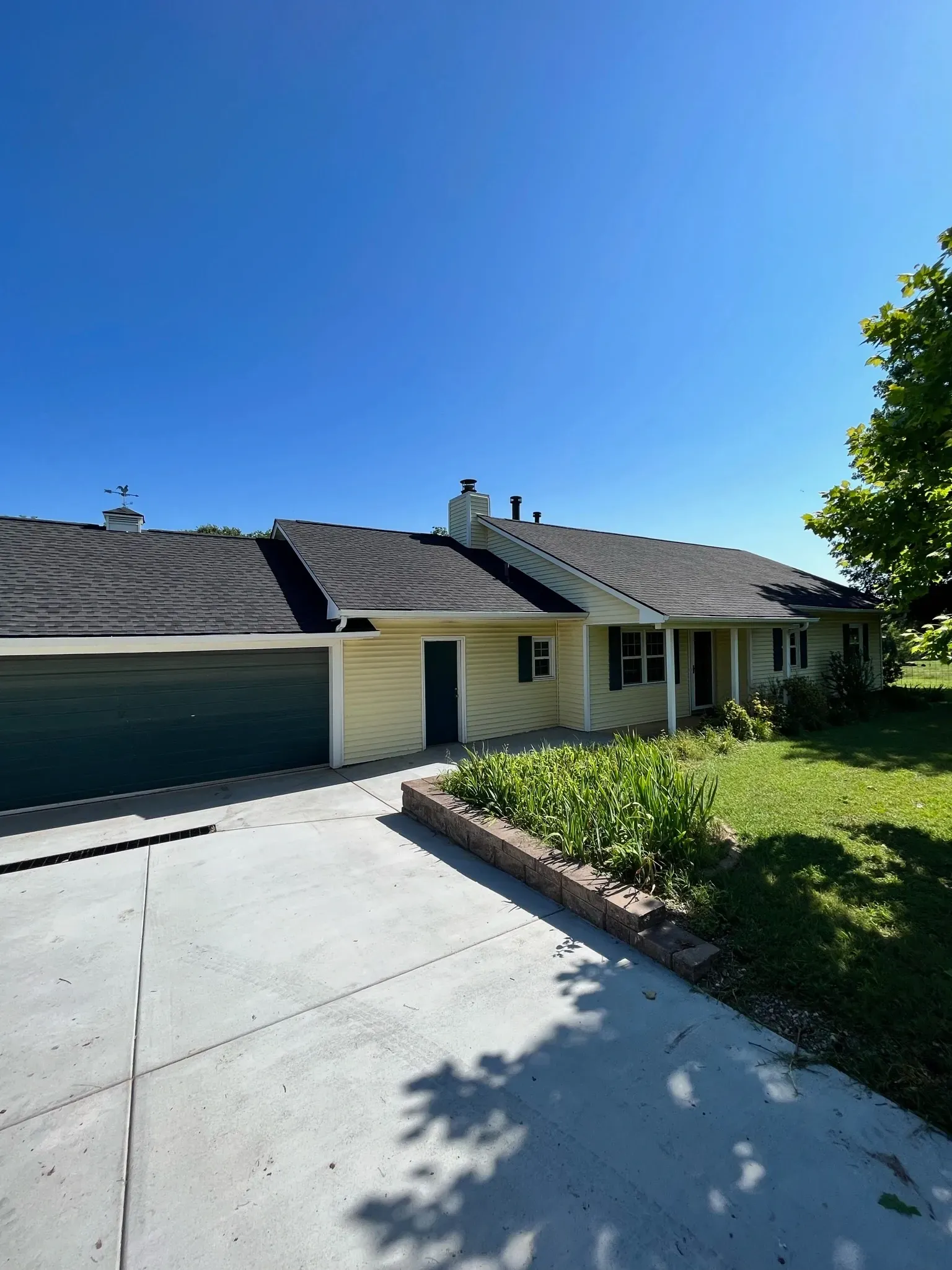 Single-story house with a garage, concrete driveway, and green lawn under a clear blue sky