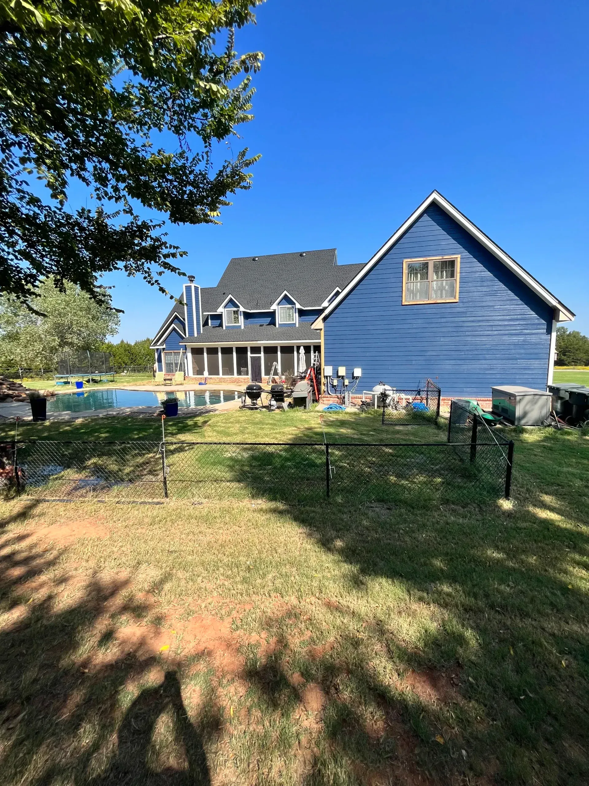 Blue two-story house with a porch, people gathered outside, and a fenced yard under a sunny sky