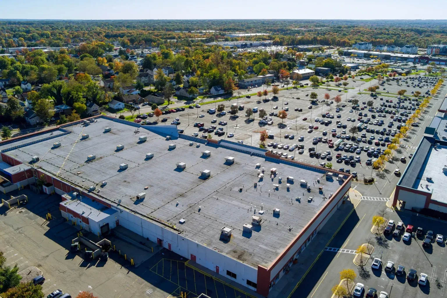 Aerial view of a large retail store and parking lot with many cars, surrounded by trees.