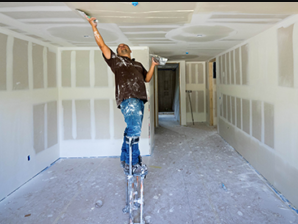 Person on a ladder painting a drywall ceiling in an unfinished room