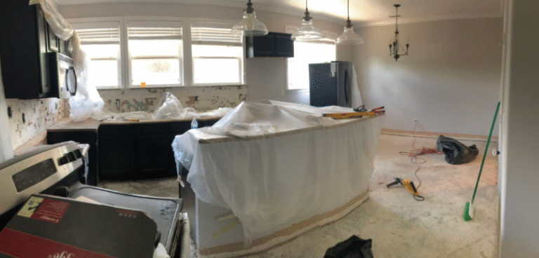 Renovated kitchen with island covered in plastic, bare floors, and tools during remodeling