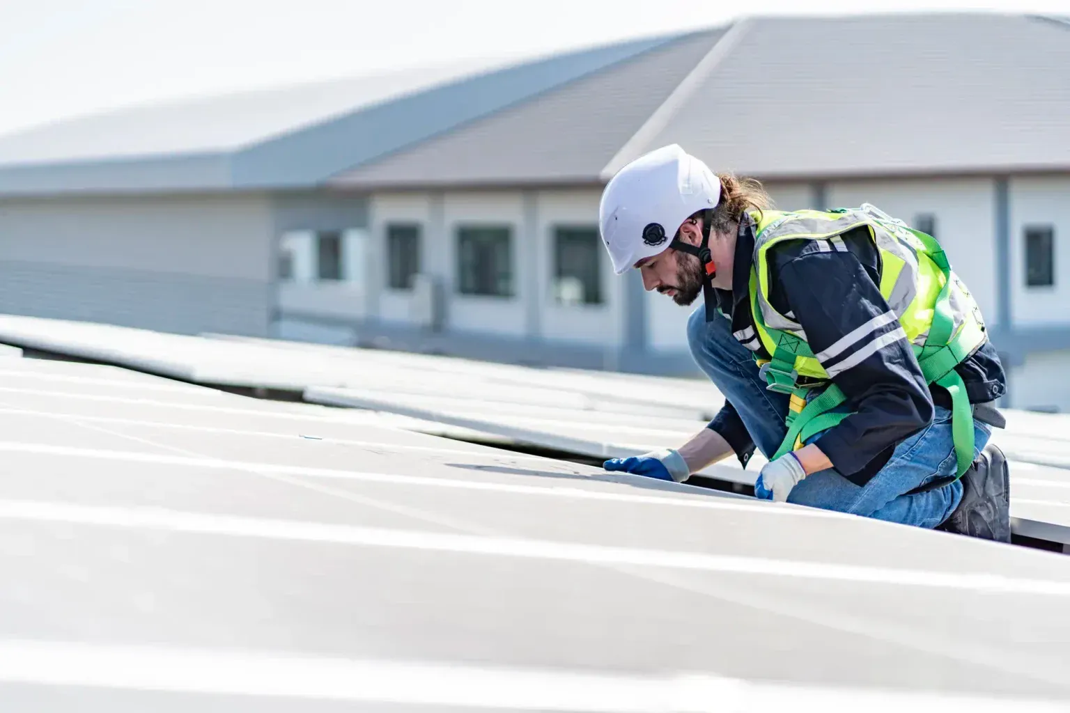 Worker in safety gear inspecting and sealing a white roof on a building