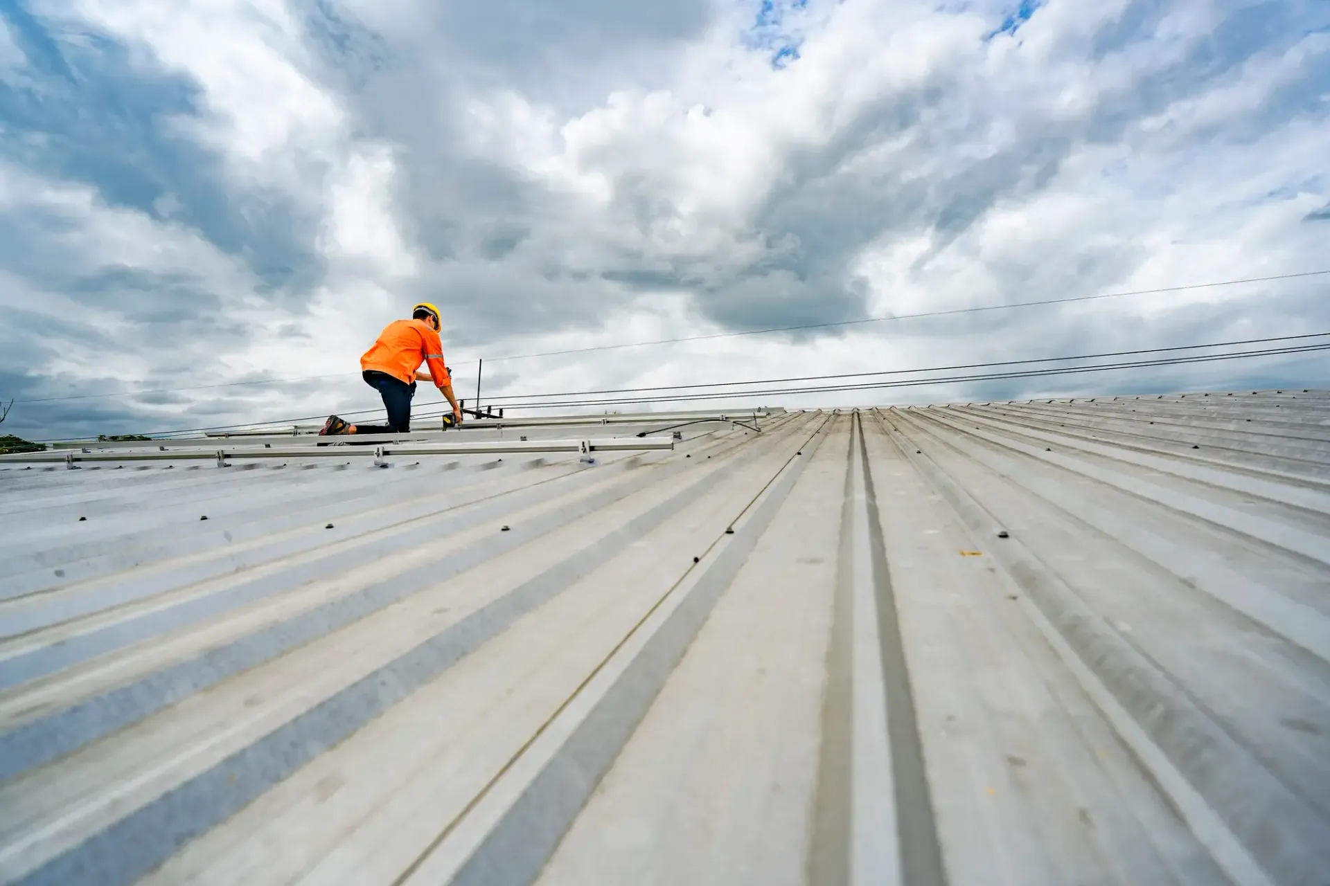Worker in orange jacket kneeling on a rooftop under a cloudy sky