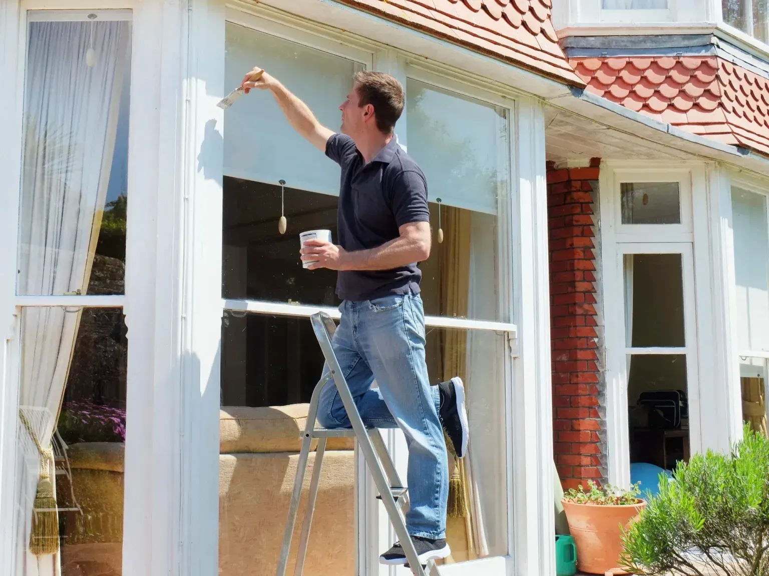 Person on a step ladder painting the white trim of a house exterior.