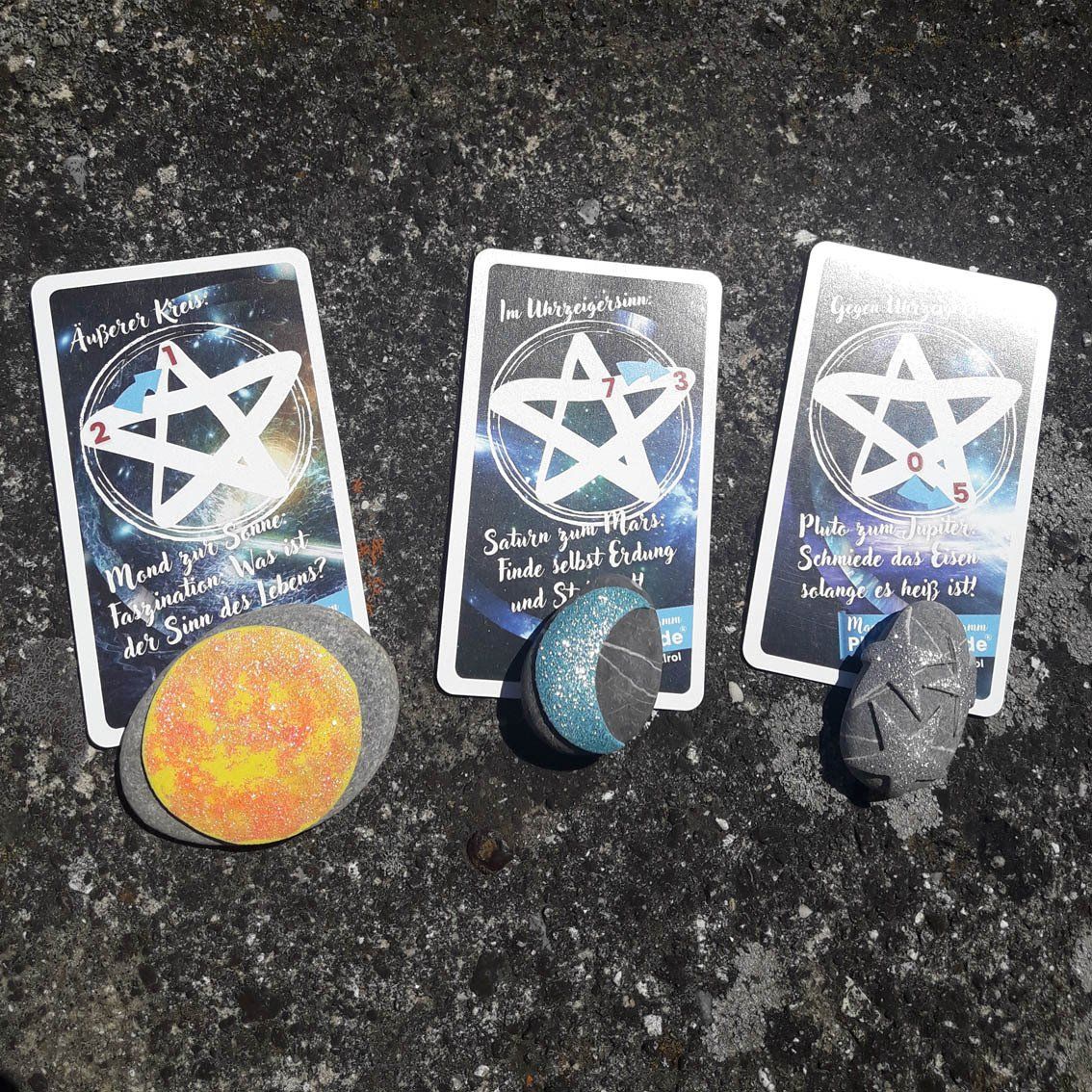 Drei Tarotkarten mit bunten Steinen und Kristallen auf dunklem, strukturiertem Untergrund.