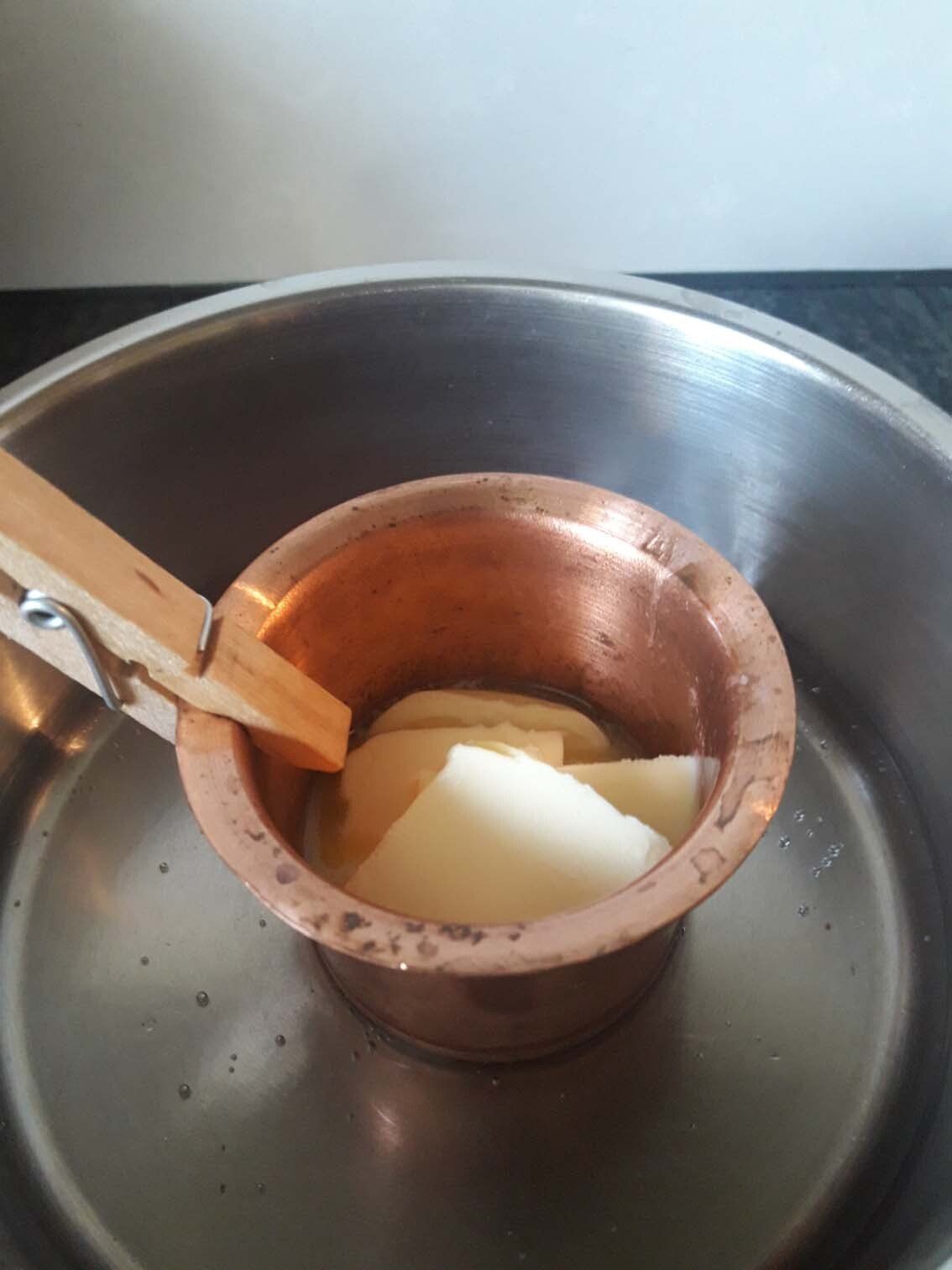 Kupfertopf mit blasser Masse in einer Metallschüssel, die mit einem Holzlöffel umgerührt wird