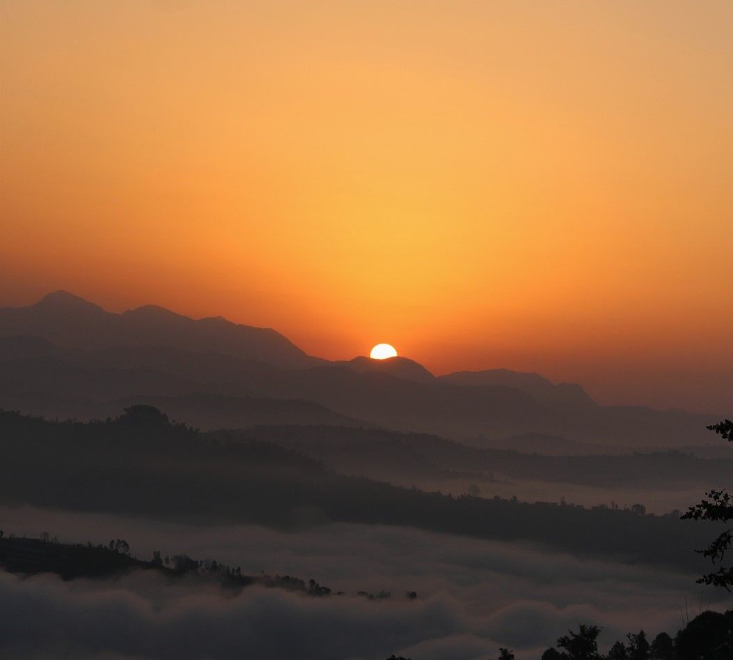 Sonnenuntergang über nebelverhangenen Bergen mit orangefarbenem Himmel und sich abzeichnenden Bergkämmen