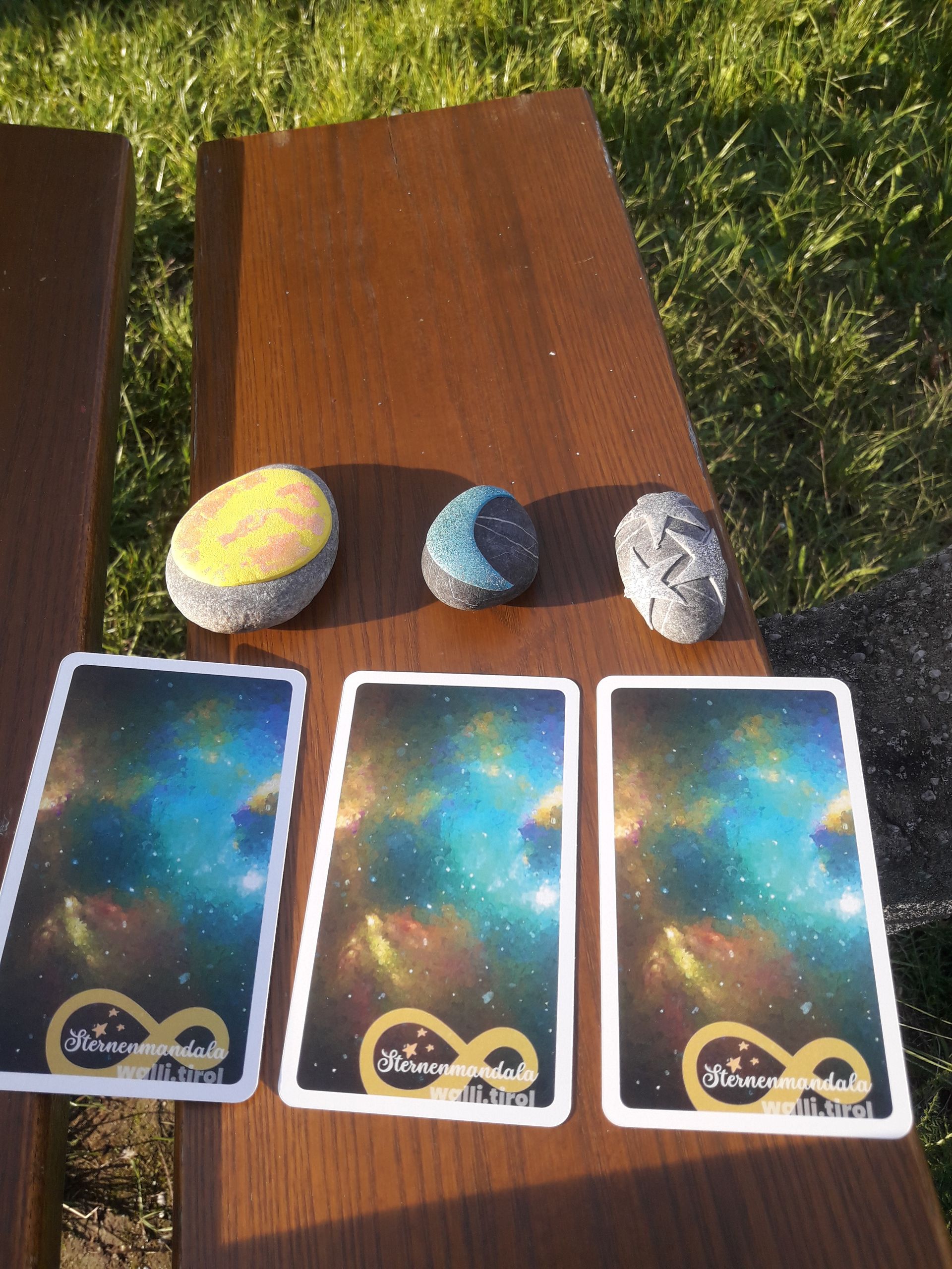 Drei Tarotkarten und drei Kristalle waren im Sonnenlicht auf einem Holztisch im Freien arrangiert.