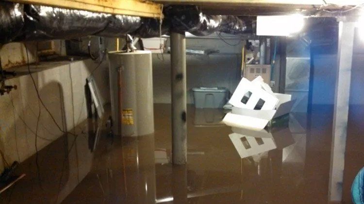 Flooded basement with standing brown water. Water heater, support beam, and debris are visible.