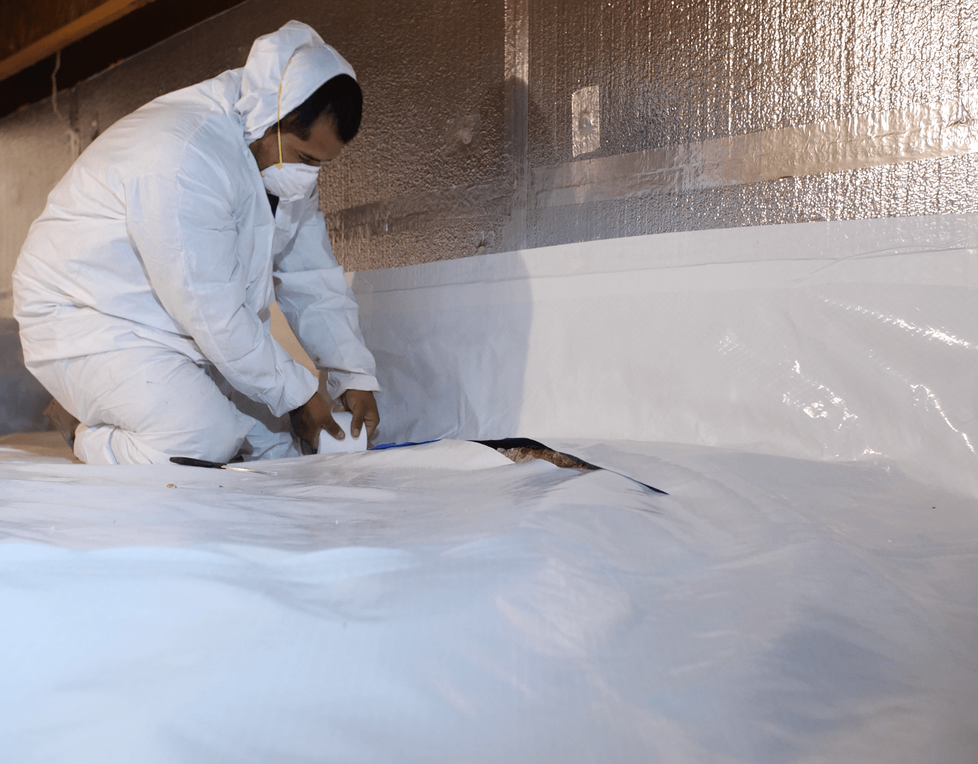 Person in protective suit installing white material in a crawl space.