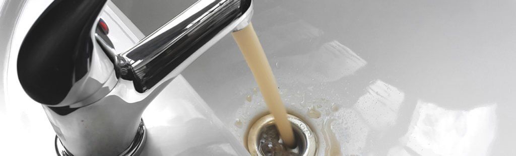 Rusty brown water flows from a chrome faucet into a white sink, likely indicating a water quality issue.