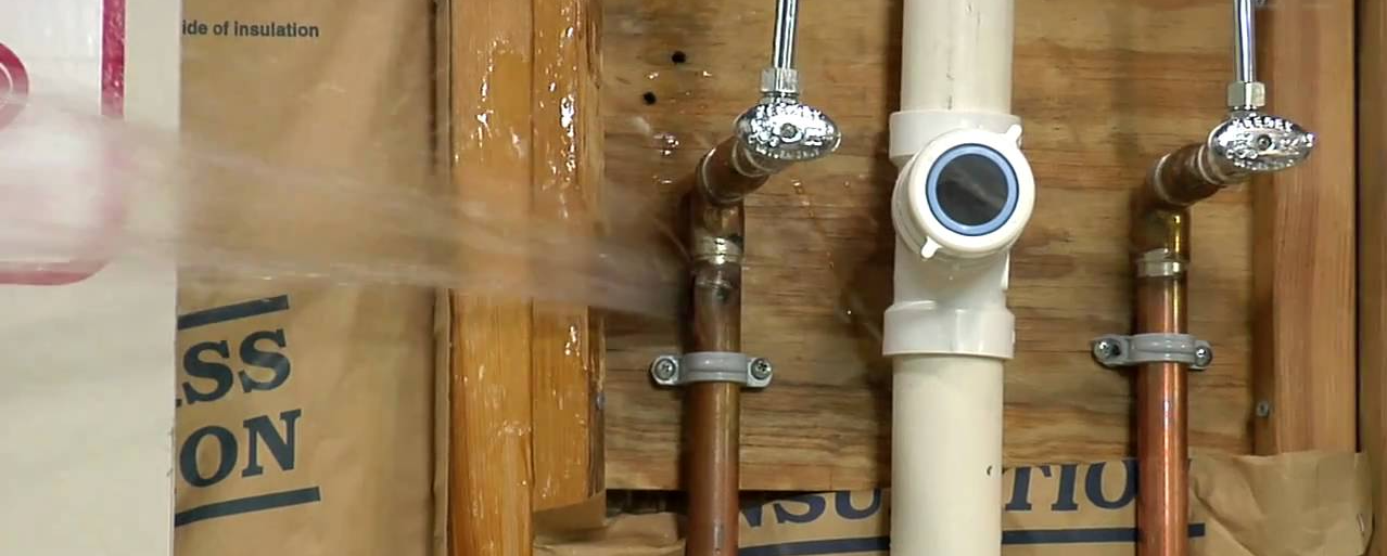 Copper pipes leaking water, with a showerhead and valve, mounted on wooden studs.