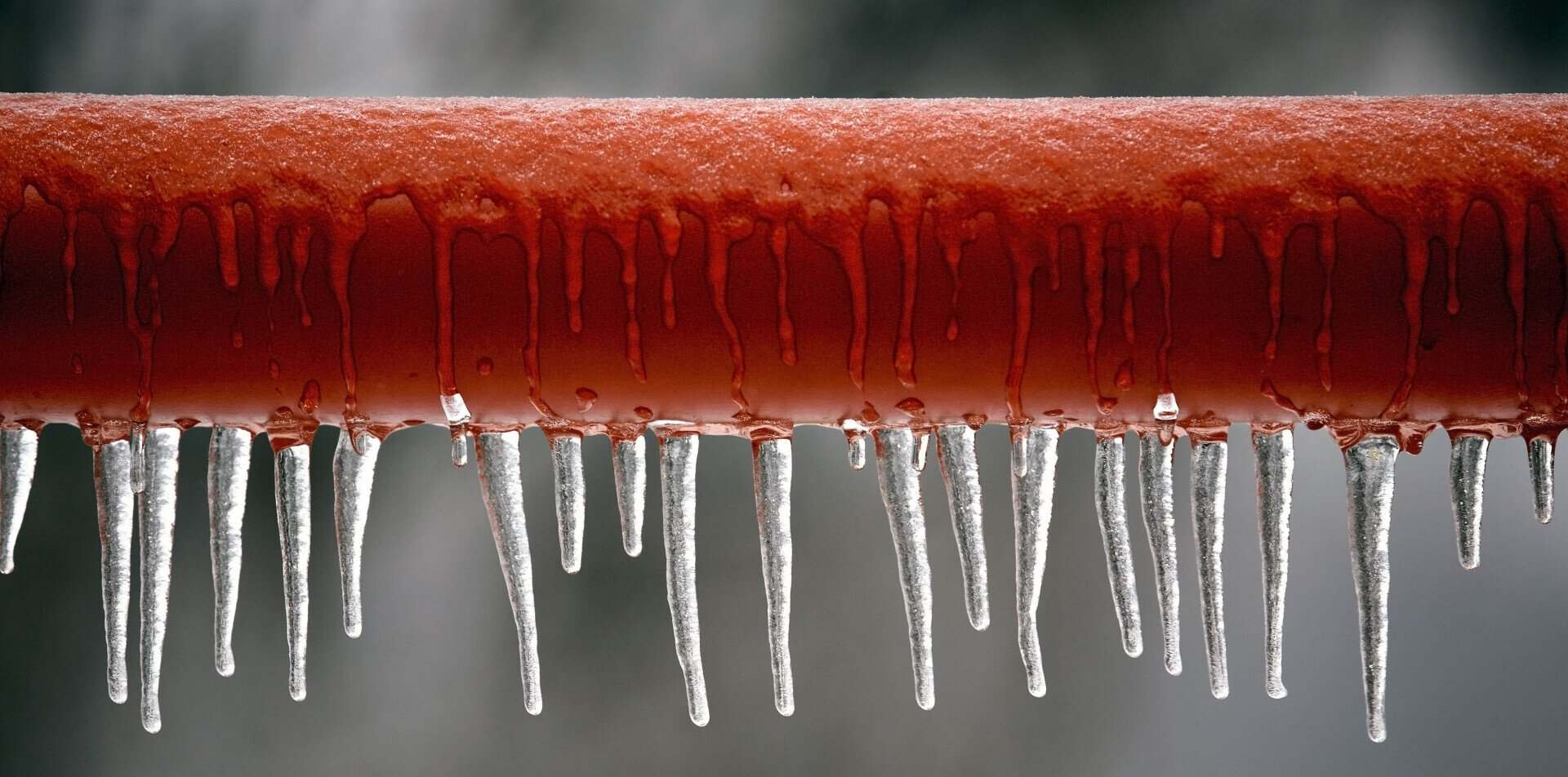 Red pipe covered in ice, with icicles hanging down. White steam rising up.