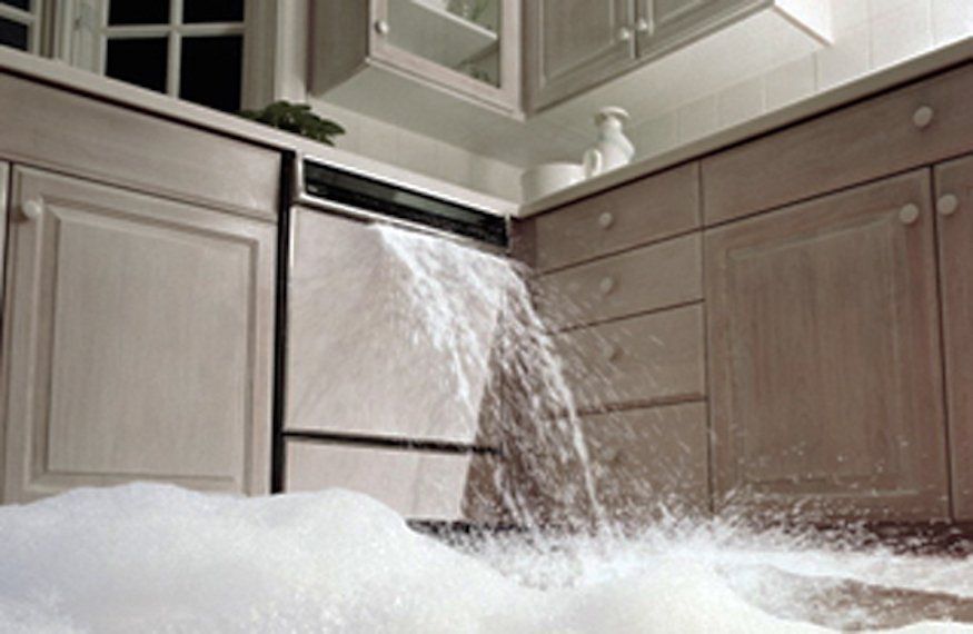 Water gushing from a dishwasher in a kitchen, flooding the floor with white soapy water.