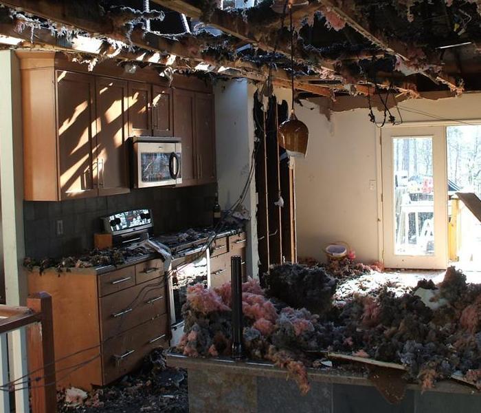 Kitchen destroyed by fire: burnt cabinets, exposed ceiling, debris on floor.