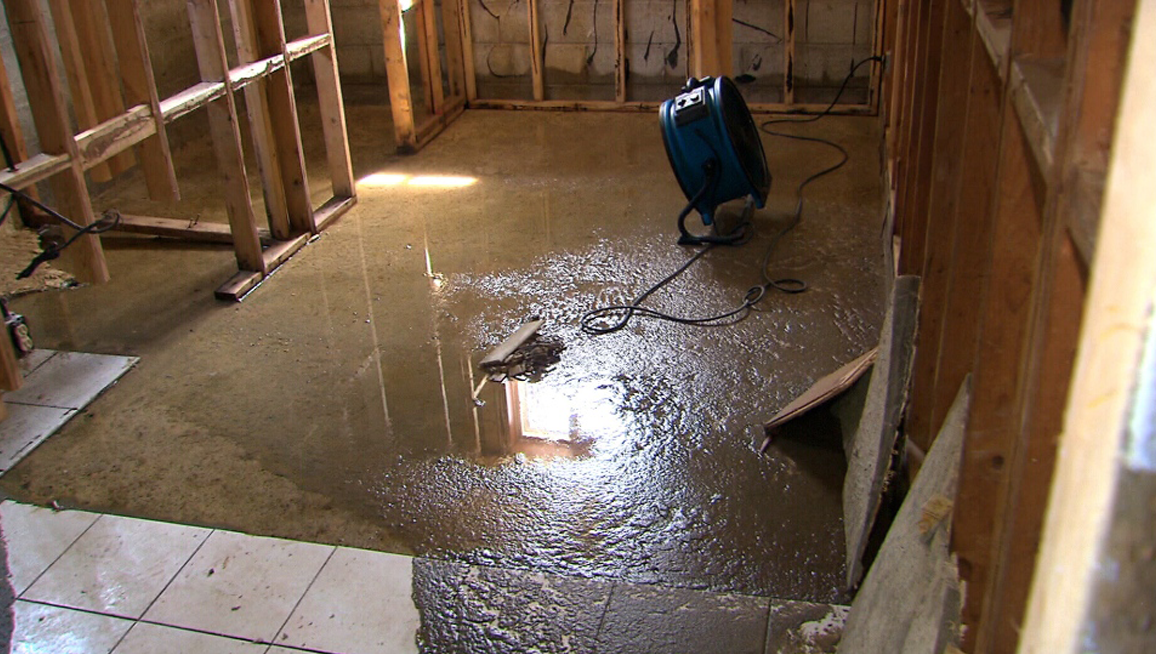 Flooded room with exposed wooden studs, a fan, and water on the floor.