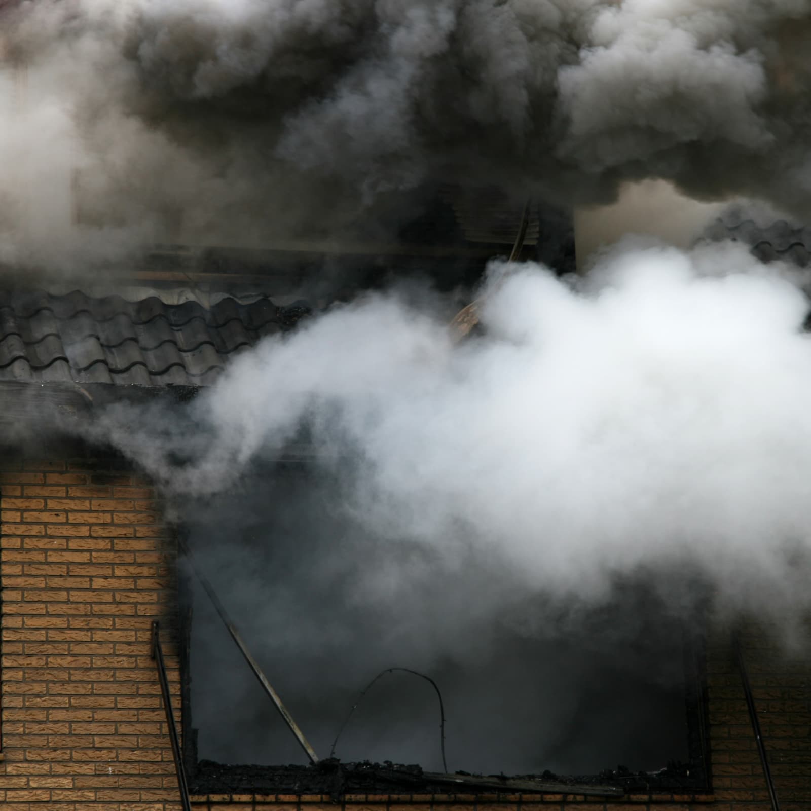 Black smoke billowing from window of burning brick building.